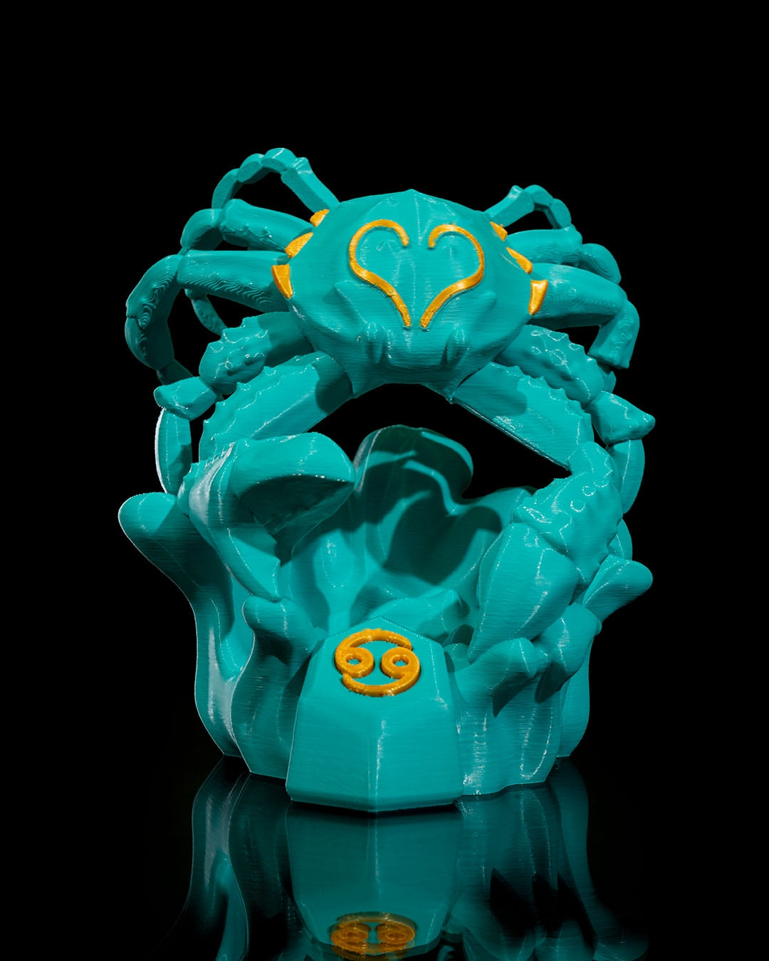 Vorderansicht der türkisen Krebs-Skulptur mit gelben Details (Astrologie-Symbol) auf schwarzem Hintergrund.