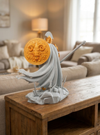 Ares-Statue Rückansicht mit wehendem Umhang und goldenem Widder-Schild, auf rustikalem Holztisch mit Lampe im Hintergrund