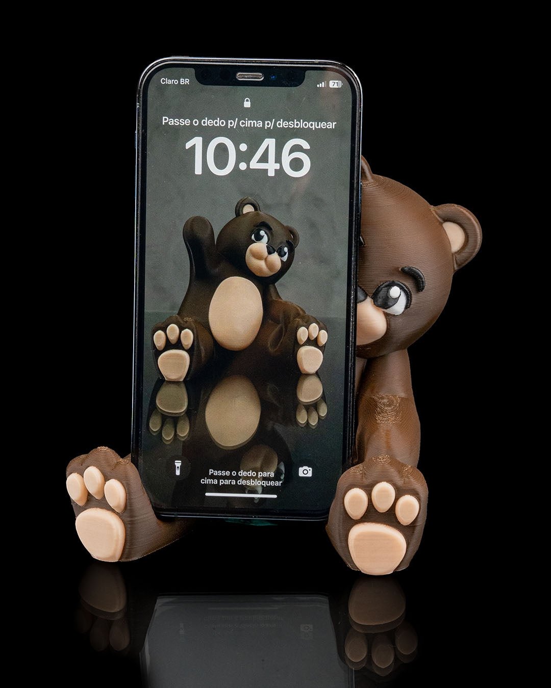Brauner Bären-Handyhalter mit eingestecktem Smartphone und sichtbarem Sperrbildschirm, Frontalansicht vor schwarzem Hintergrund