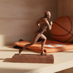 Basketball-Statue in Kupfer-Bronze-Optik auf Holzregal, Seitenansicht im Laufschritt, unscharfer Hintergrund mit Basketball und Trikot – Münch3D