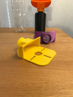 Nahaufnahme von zwei Bohrstaub-Fangtrichtern in Gelb und Lila auf einem Holztisch, im Hintergrund die schwarze Sammelflasche mit orangem Trichter