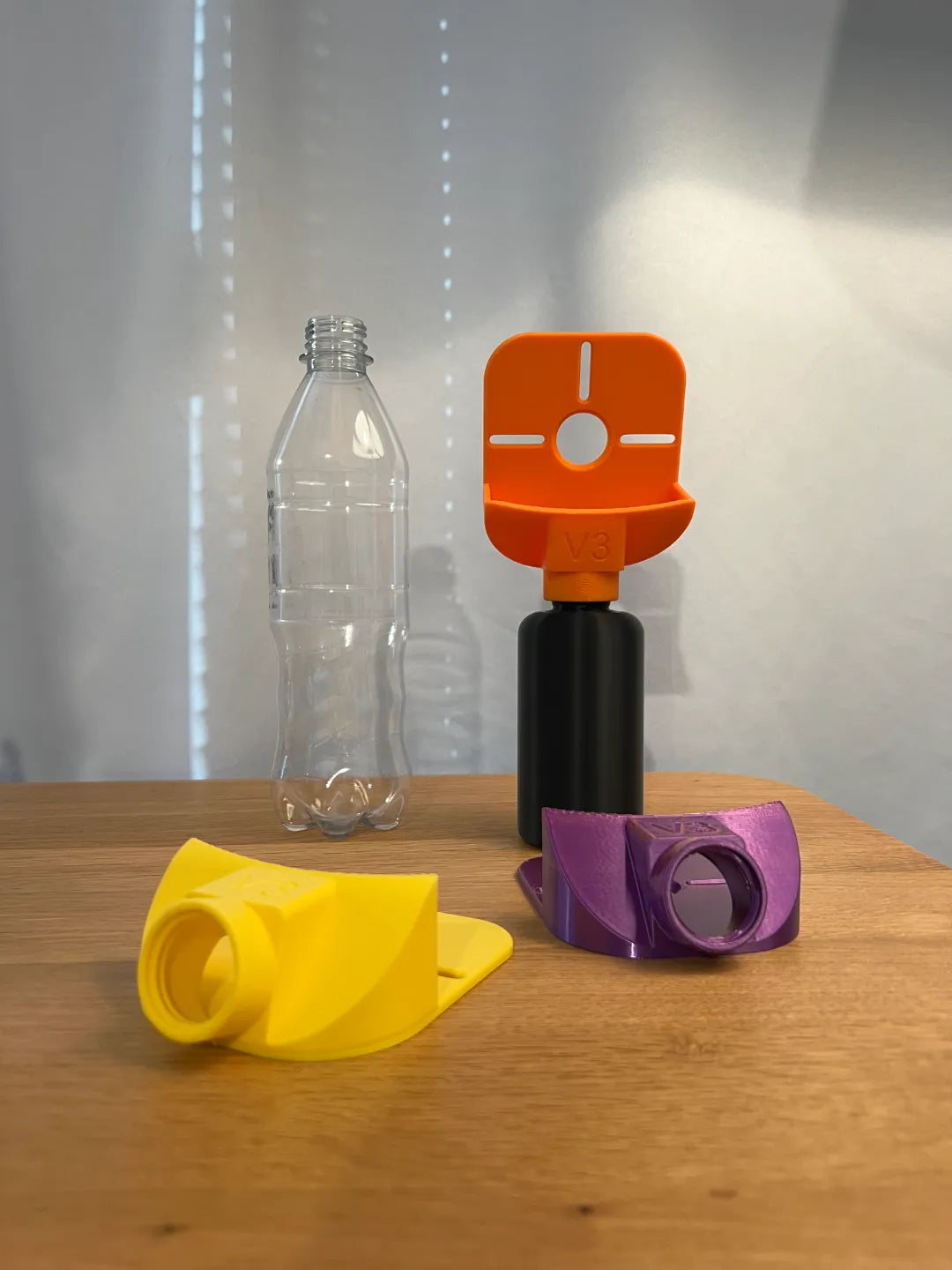 Bohrstaub-Fangtrichter-Set: schwarze gedruckte Sammelflasche mit montiertem orangem Trichteraufsatz, daneben lose Trichteraufsätze in Gelb und Lila sowie eine leere durchsichtige PET-Flasche im Hintergrund