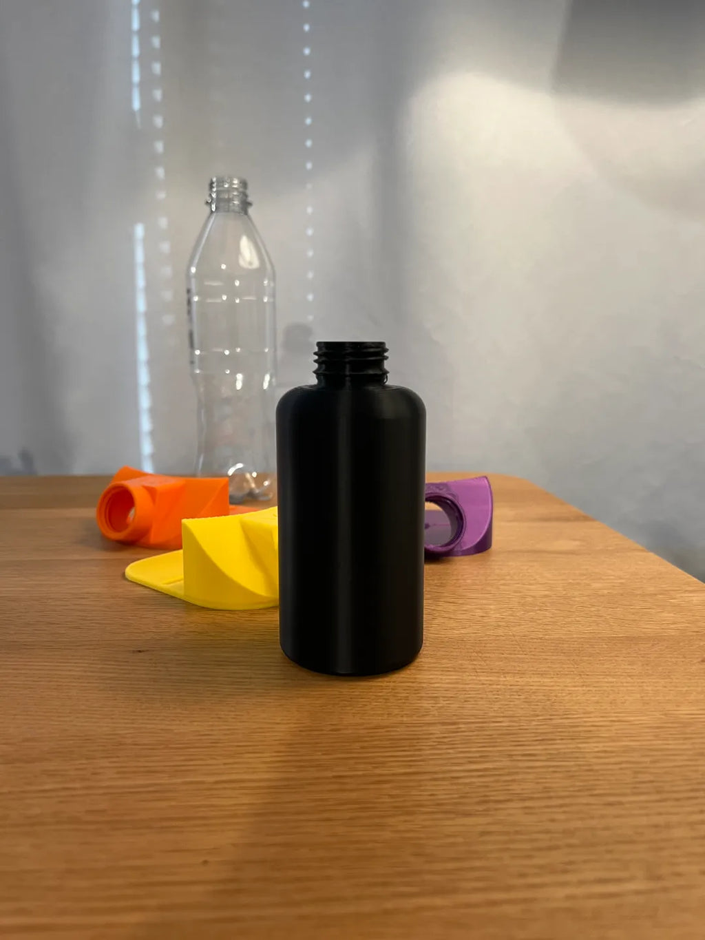 Schwarze gedruckte Sammelflasche in Nahaufnahme mit offenem Gewinde, im Hintergrund unscharf Trichteraufsätze und Getränkeflaschen