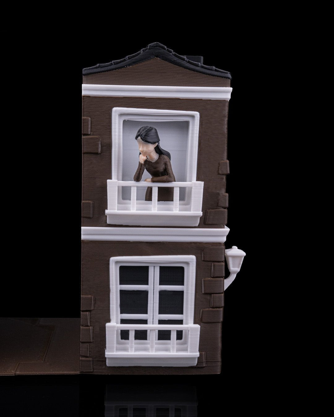Braune Hausfassaden-Buchstütze mit Frauenfigur auf dem Balkon im Obergeschoss und leerem Fenster im Erdgeschoss, Wandlaterne, freigestellt vor schwarzem Hintergrund