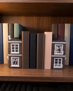Buchstützen-Set Romance in Between im Einsatz zwischen mehreren Büchern im Regal, Katze auf dem Dach und Charaktere in den Fenstern beider Hausfassaden