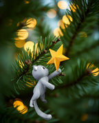 Christbaumspitze Katze kletternd mit goldenem Stern, Seitenansicht zwischen echten Tannenzweigen mit warmem Lichterglanz