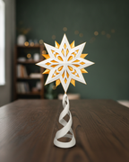 Christbaumspitze Groß, 24 cm, mit weiß-goldenem Stern auf weißer Spirale, aufgestellt auf einem dunklen Holztisch, im Hintergrund ein unscharfes Zimmer mit grüner Wand, Regal und Lichterkette
