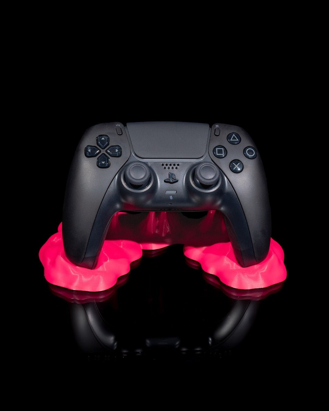 Schwarzer Gaming-Controller in pinkfarbenem Sticky-Splash-Controller-Ständer, Frontalansicht vor schwarzem Hintergrund