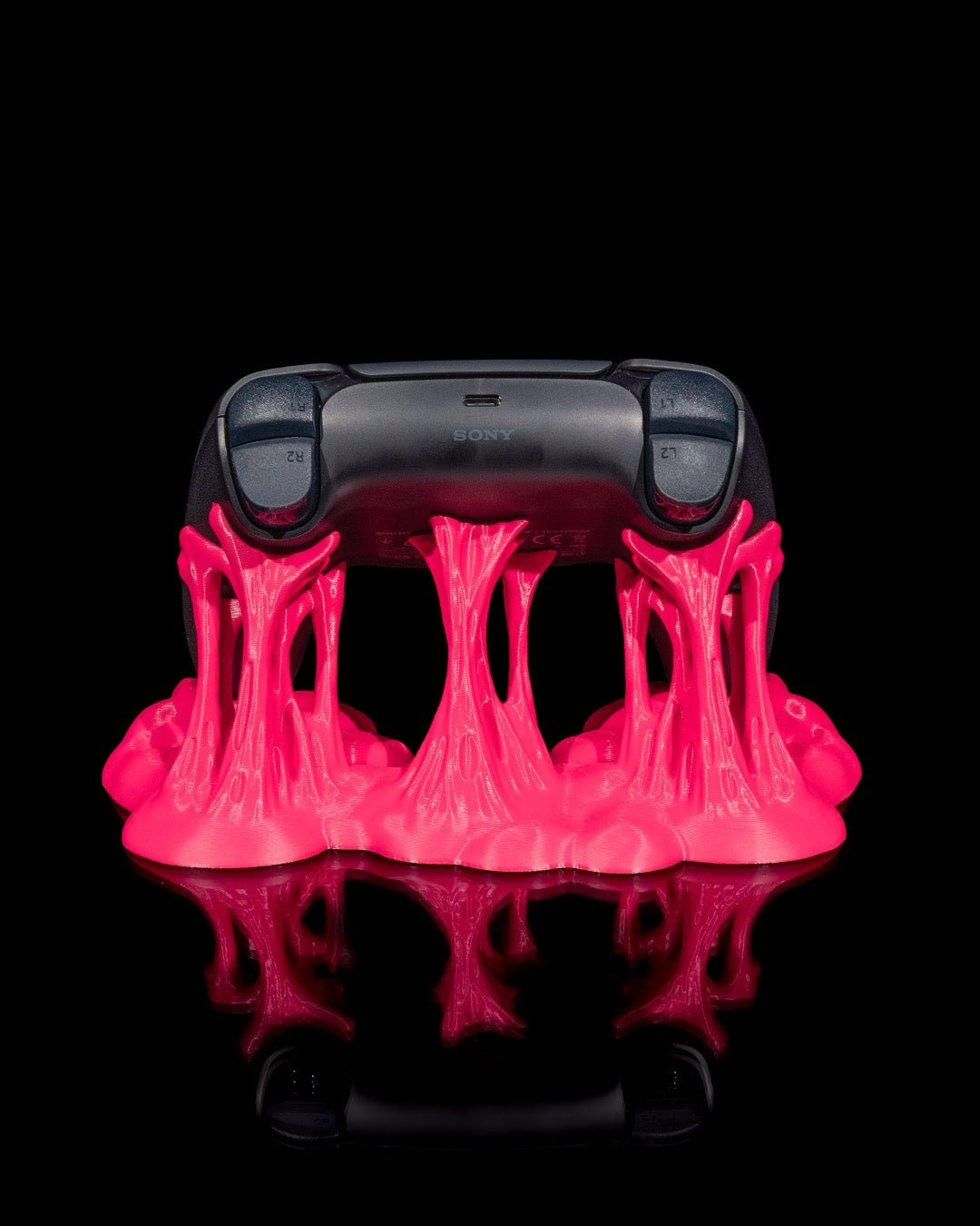 Schwarzer Gaming-Controller von hinten in pinkfarbenem Sticky-Splash-Ständer, Rückseite mit Schultertasten sichtbar, vor schwarzem Hintergrund
