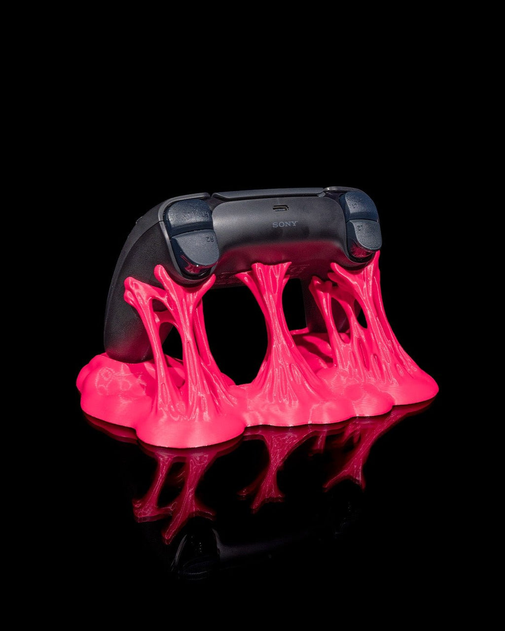 Schwarzer Gaming-Controller schräg von der Seite in pinkfarbenem Sticky-Splash-Ständer vor schwarzem Hintergrund
