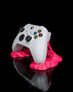 Weißer Gaming-Controller schräg von oben in pinkfarbenem Sticky-Splash-Ständer, Nahaufnahme vor schwarzem Hintergrund