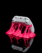 Weißer Gaming-Controller von hinten in pinkfarbenem Sticky-Splash-Ständer, Rückseite mit Schultertasten sichtbar, vor schwarzem Hintergrund