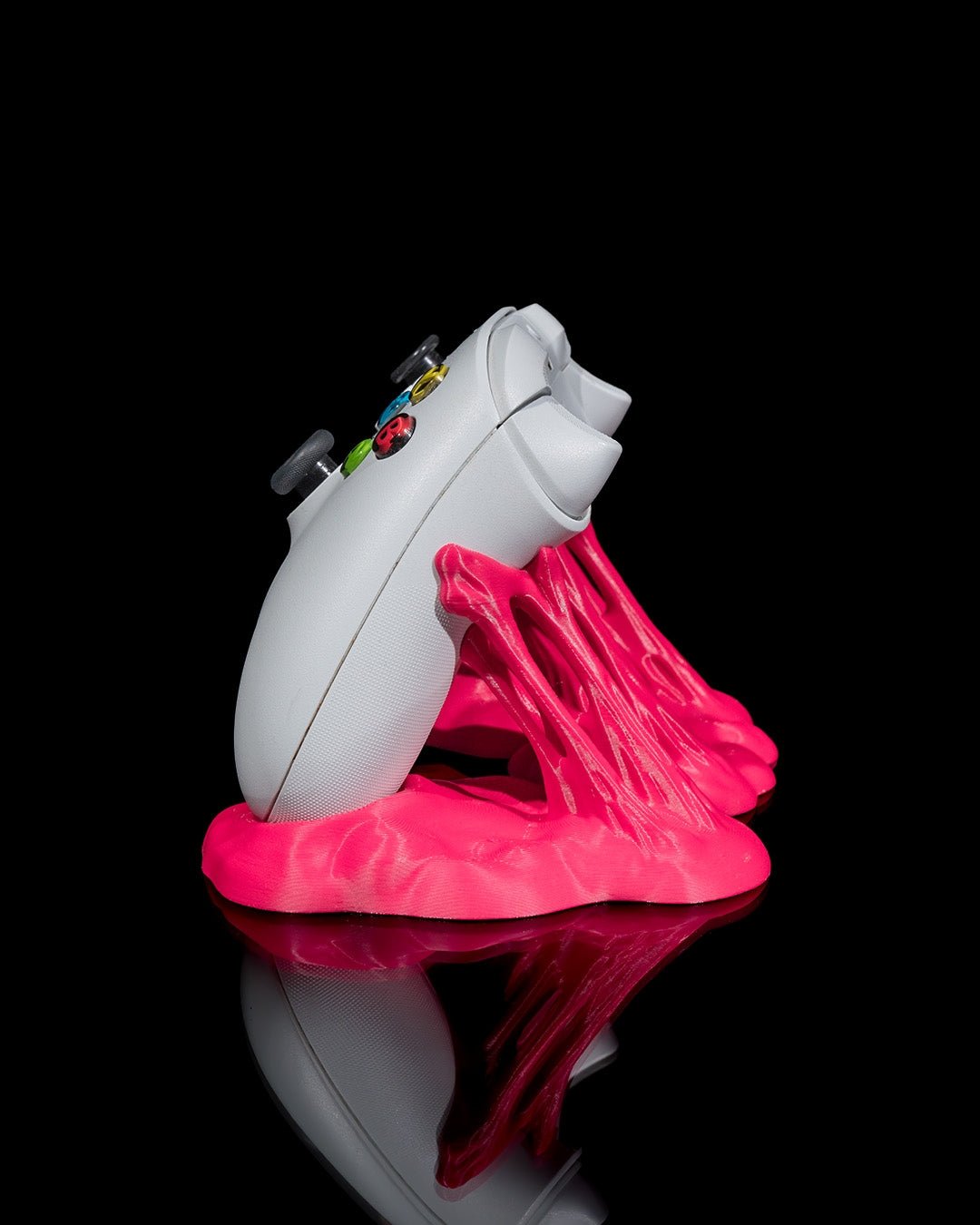 Weißer Gaming-Controller seitlich fotografiert in pinkfarbenem Sticky-Splash-Ständer vor schwarzem Hintergrund