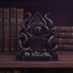 Schwarze Cthulhu-Schmuckschale mit Ringen und Fledermaus-Ohrringen in der Ablageschale, auf einem Bücherregal mit ledergebundenen Büchern