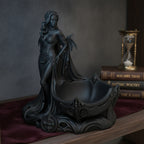 Gothic-Dämonin-Statue mit Fledermausflügeln und Dornenkrone, Frontalansicht mit integrierter Schmuckschale auf einem Bücherregal neben einer Sanduhr