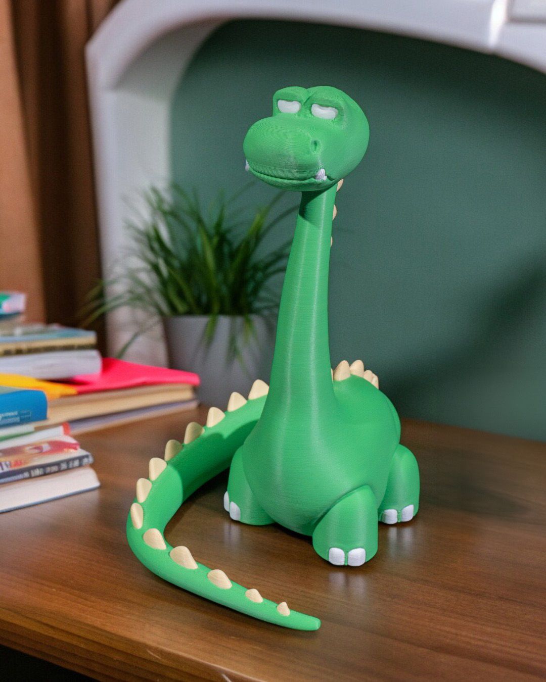 Grüner Dino-Handyhalter ohne Smartphone auf Holzschreibtisch, mit Büchern, Pflanze und grüner Wand im Hintergrund