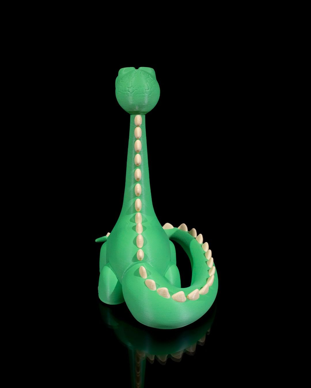 Grüner Dino-Handyhalter ohne Smartphone, Rückansicht mit Stachelreihe am Hals und gezähntem Schwanzring, schwarzer Hintergrund