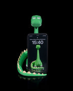 Grüner Dino-Handyhalter mit eingestecktem Smartphone und sichtbarem Sperrbildschirm, Frontalansicht mit gezähntem Schwanzring vor schwarzem Hintergrund