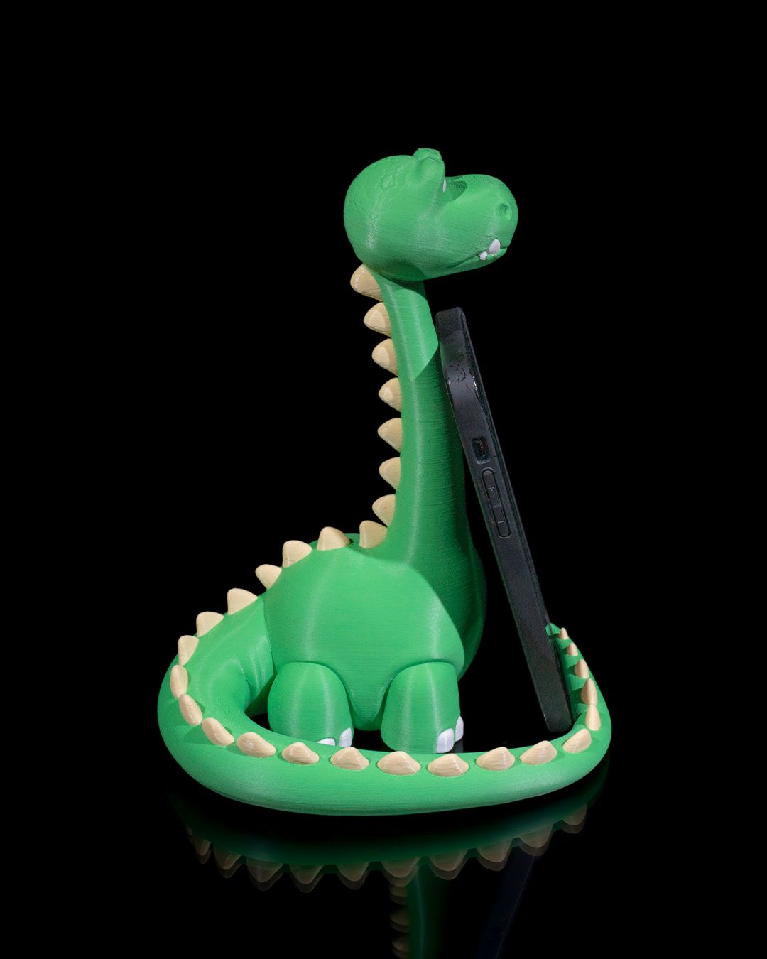 Grüner Dino-Handyhalter mit eingestecktem Smartphone, Rückseite des Handys sichtbar, seitliche Ansicht vor schwarzem Hintergrund