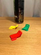 Drei Dosenöffner-Clips in Gelb, Rot und Grün auf Holztisch, Getränkedose im Hintergrund