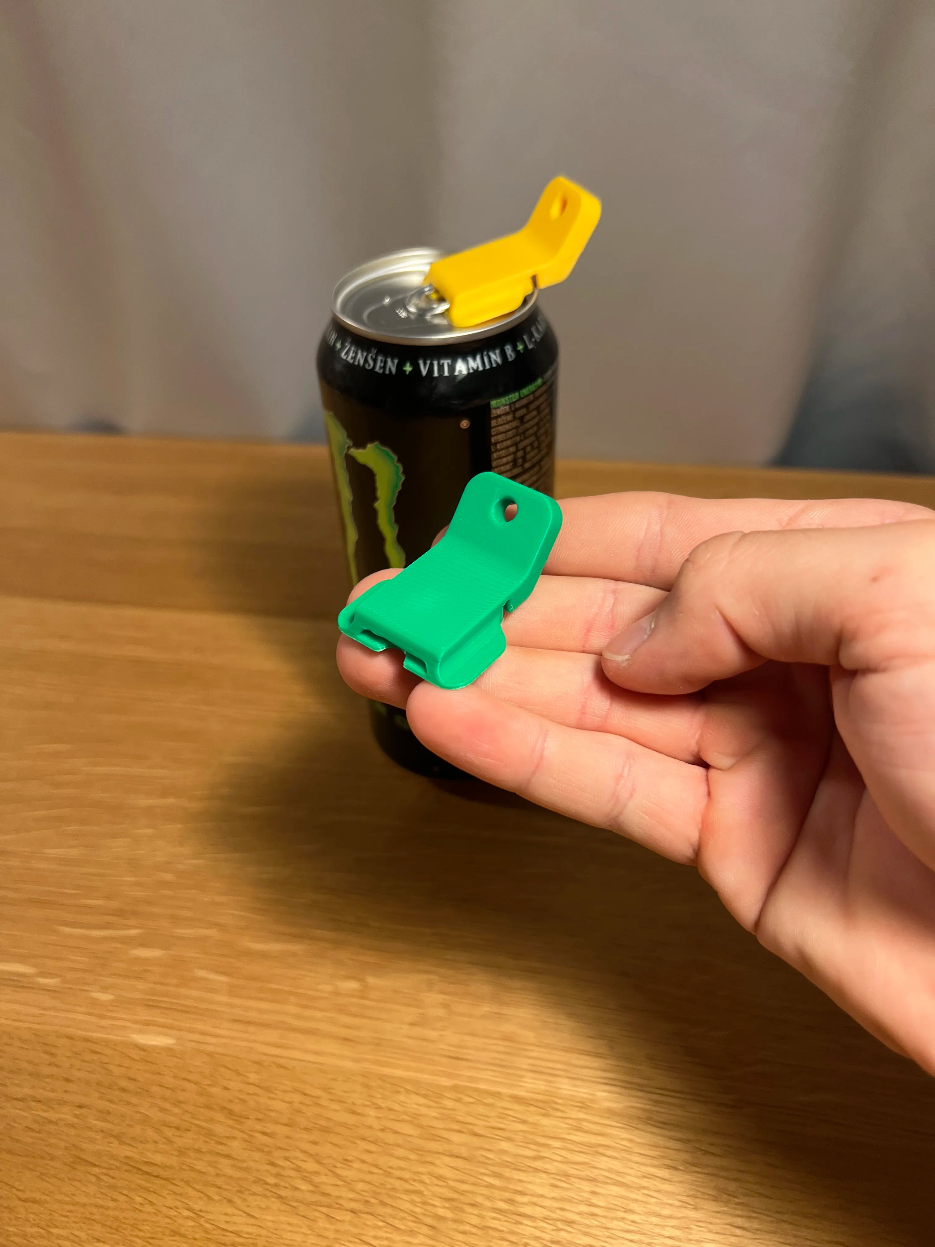 Grüner Dosenöffner-Clip in der Hand, im Hintergrund eine Dose mit aufgesetztem gelben Clip
