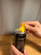 Gelber Dosenöffner-Clip hebelt die Aufreißlasche einer Energy-Drink-Dose in Großaufnahme auf