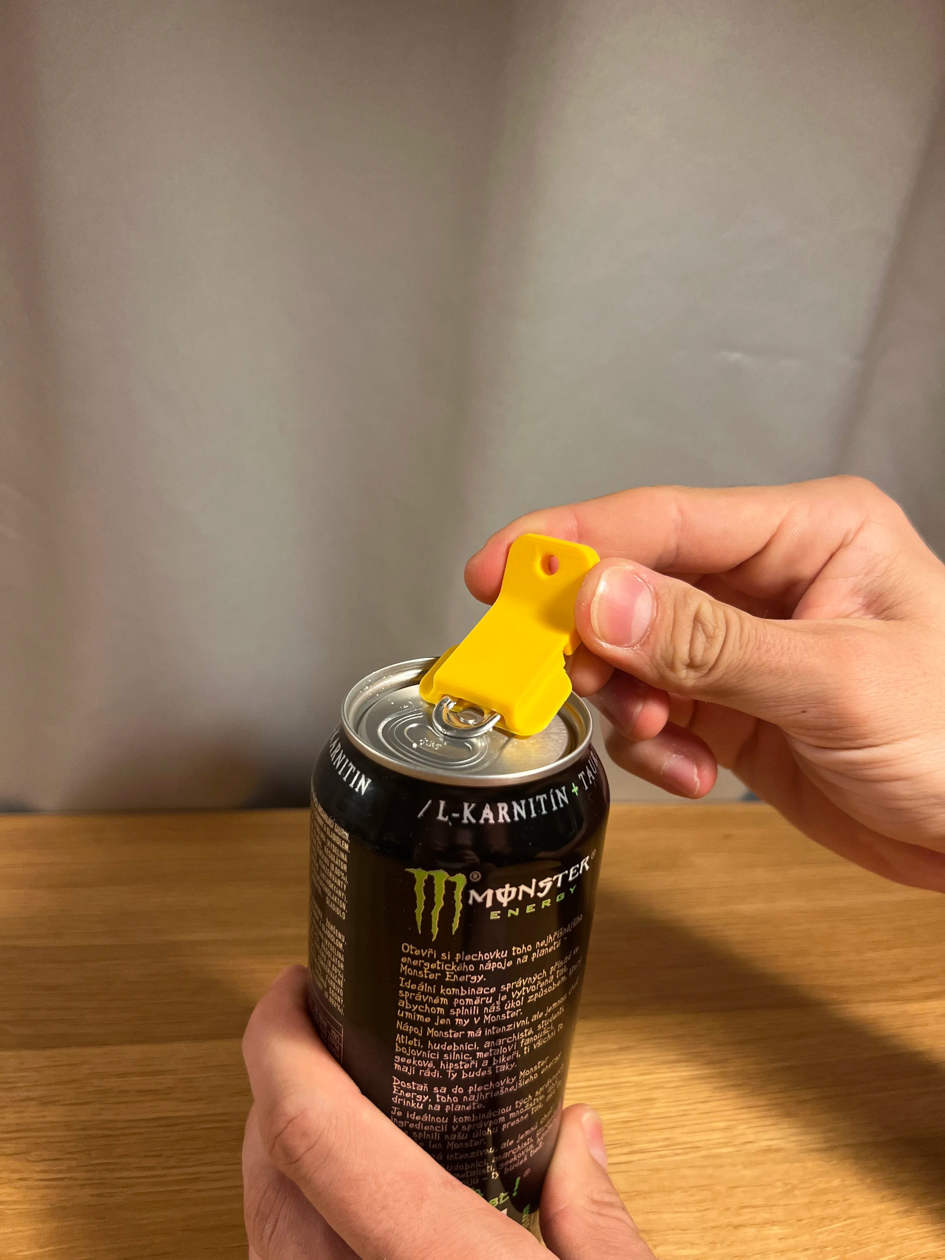 Gelber Dosenöffner-Clip hebelt die Aufreißlasche einer Energy-Drink-Dose in Großaufnahme auf