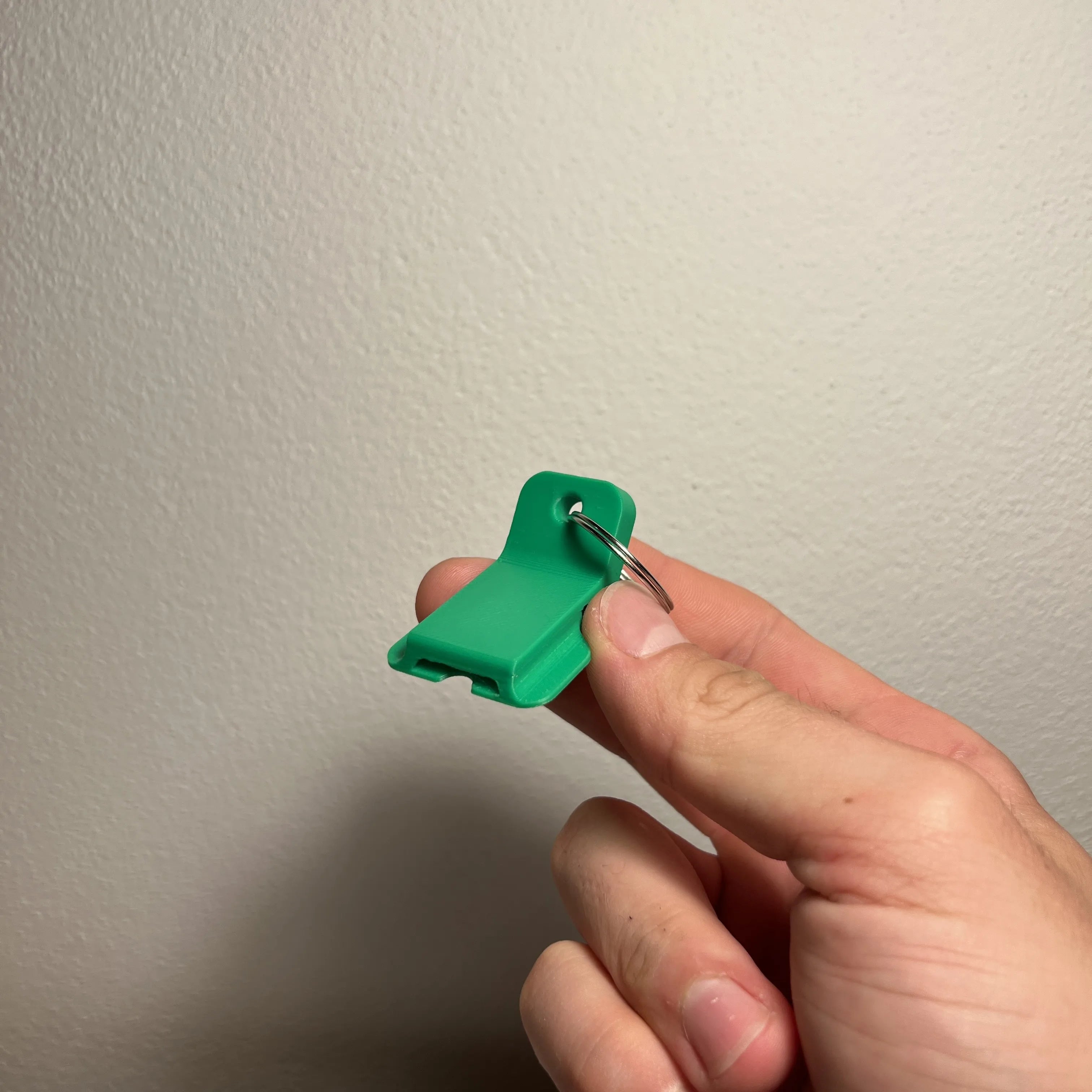 Grüner Dosenöffner-Clip an einem Schlüsselring in der Hand vor heller Wand