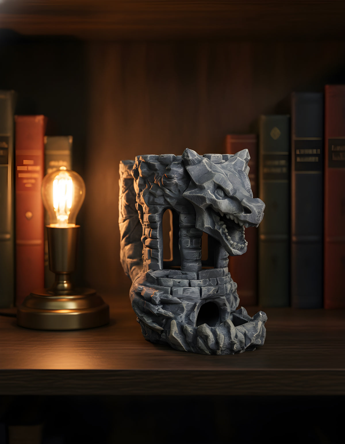 Drachen-Festungs-Würfelturm unbemalt in Silbergrau, Seitenansicht auf dunklem Holz-Bücherregal zwischen gebundenen Fantasy-Romanen, warmes Leselampenlicht von links