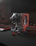 Drachen-Festungs-Würfelturm unbemalt in Silbergrau, Frontalansicht auf mattschwarzem Gaming-Schreibtisch neben roter RGB-Tastatur, drei Würfel liegen am Sockel verstreut