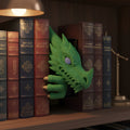 Grüner Drachenkopf Book Nook zwischen dunklen Fantasy-Buchrücken im Bücherregal, warmes Leselampenlicht