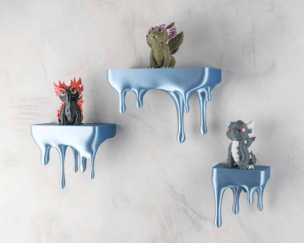 Drei blaue Tropfen-Wandregale mit Drachenfiguren (rot, oliv, grau) an heller Steinwand, Nahaufnahme
