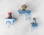 Drei blaue Tropfen-Wandregale mit je einer handbemalten Drachenfigur (rot, oliv, grau) an heller Steinwand, Weitwinkel-Ansicht