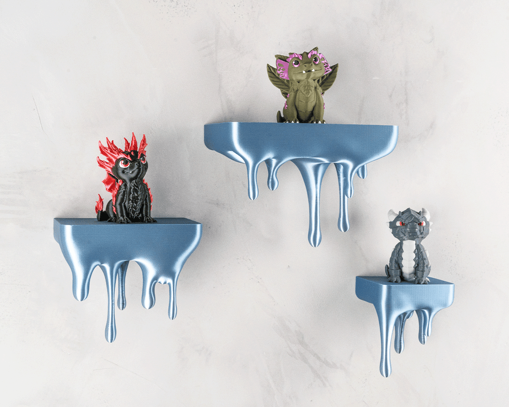 Drei blaue Tropfen-Wandregale mit Drachenfiguren (rot, oliv, grau) an heller Steinwand, etwas näher herangezoomt