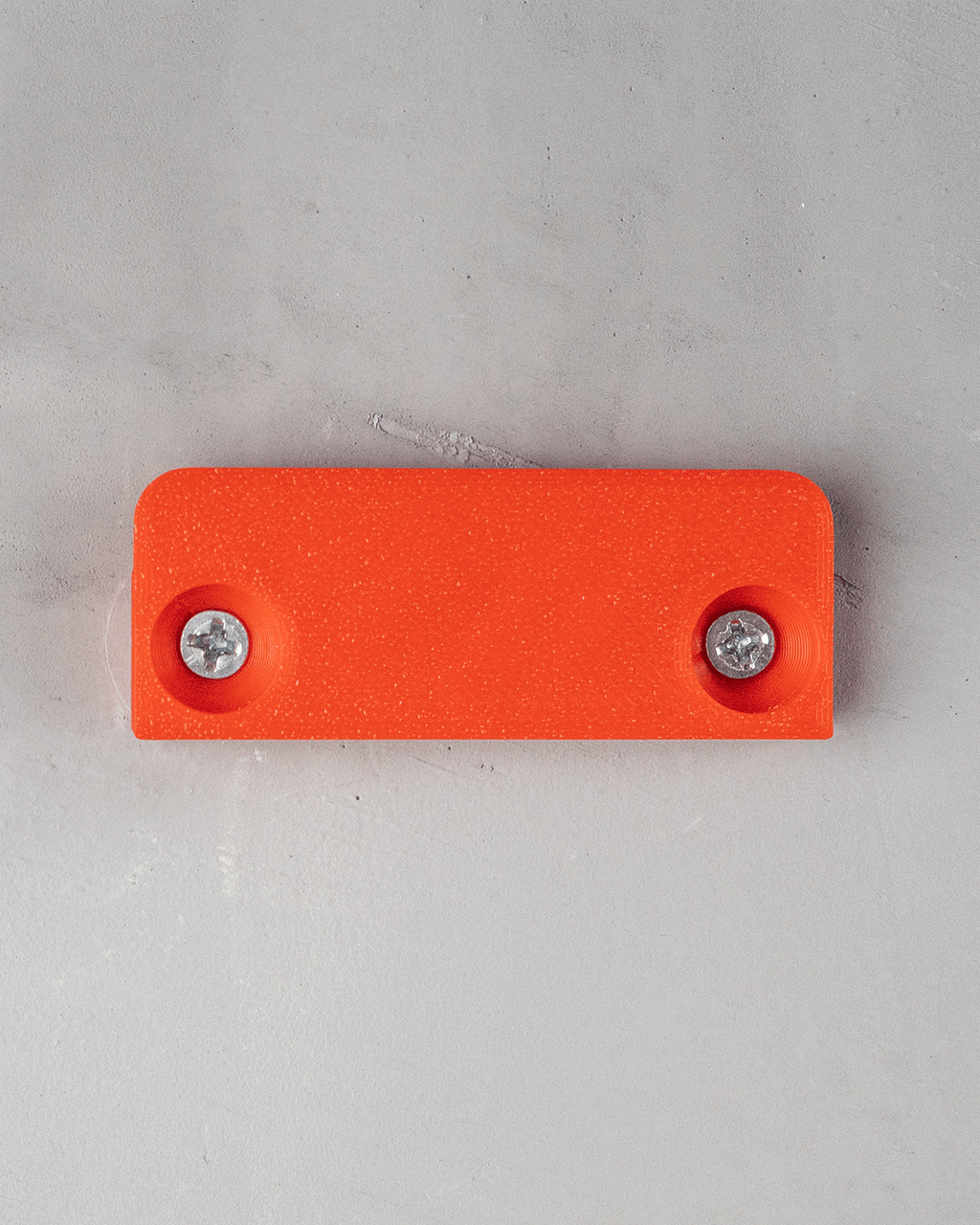 Rechteckige Montageplatte eines Tropfen-Wandregals in Orange mit zwei eingeschraubten Schrauben, Draufsicht an Wand