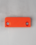 Rechteckige Montageplatte eines Tropfen-Wandregals in Orange mit zwei eingeschraubten Schrauben, Draufsicht an Wand