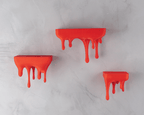 Drei Wandregale im Tropfen-Design in Rot-Orange, montiert an heller Steinwand, ohne Deko