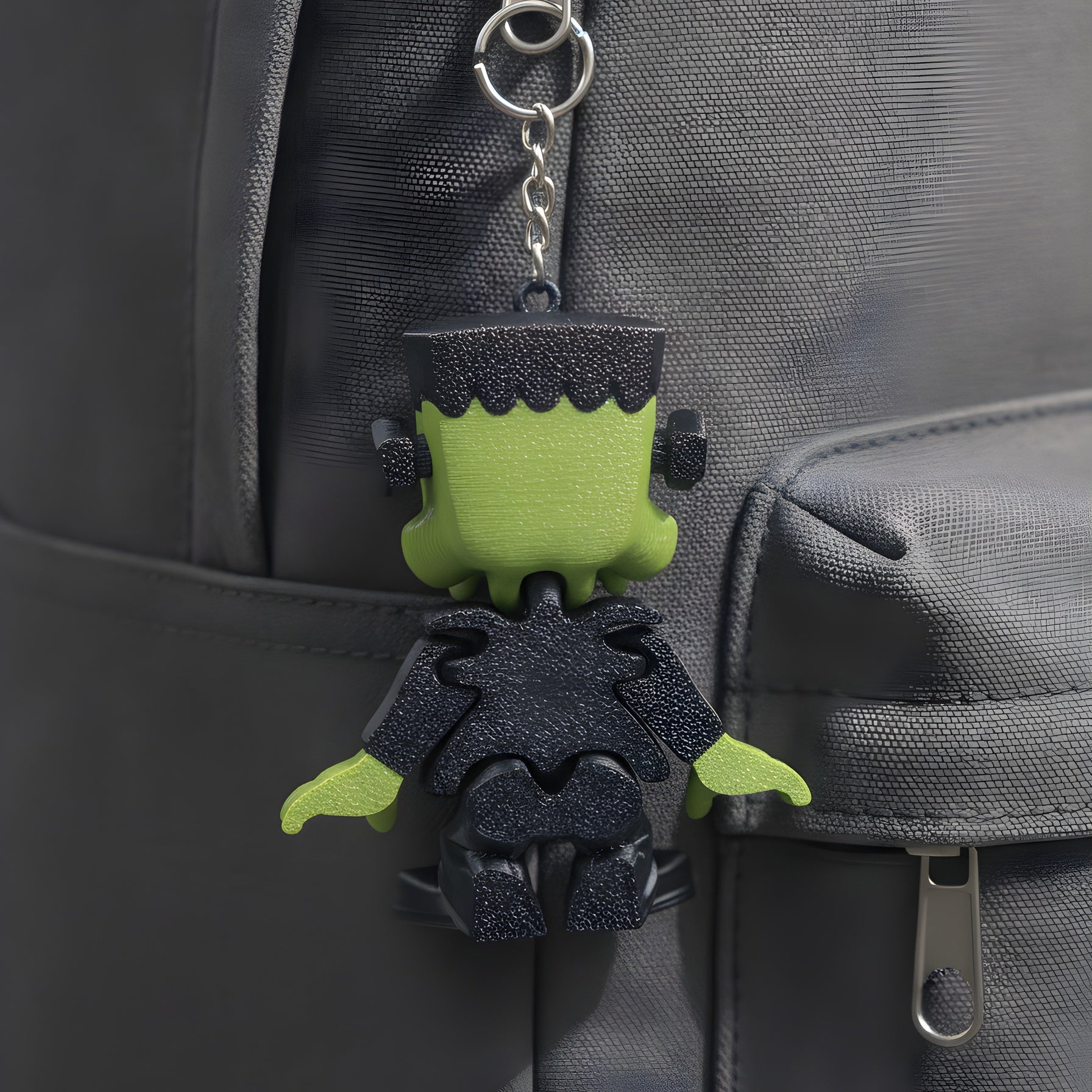Frankenstein-Schlüsselanhänger befestigt am Reißverschluss eines grauen Rucksacks, Rückansicht im Alltag.