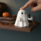 Geist-Figur mit Peace-Zeichen in dynamischer Pose, Hand hält die Figur zum Größenvergleich, Herbstdeko im Hintergrund
