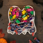 Geister-Süßigkeitenschale von oben, gefüllt mit bunten verpackten Bonbons und Lutschern als Halloween-Süßigkeitenschale