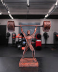 Handbemalte Gewichtheber-Statue in Kupfer-Optik, 3D-Druck im Fitnessstudio auf dunklem Tisch, unscharfer Gym-Hintergrund – Münch3D