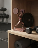 Gewichtheber-Statue in Kupfer-Optik im Ausfallschritt mit großer Gewichtsscheibe über dem Kopf, auf Holzregal im Home Gym neben Kurzhanteln – Münch3D