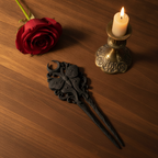 Schwarze Gothic-Haarnadel im Flatlay von oben neben Kerze und roter Rose