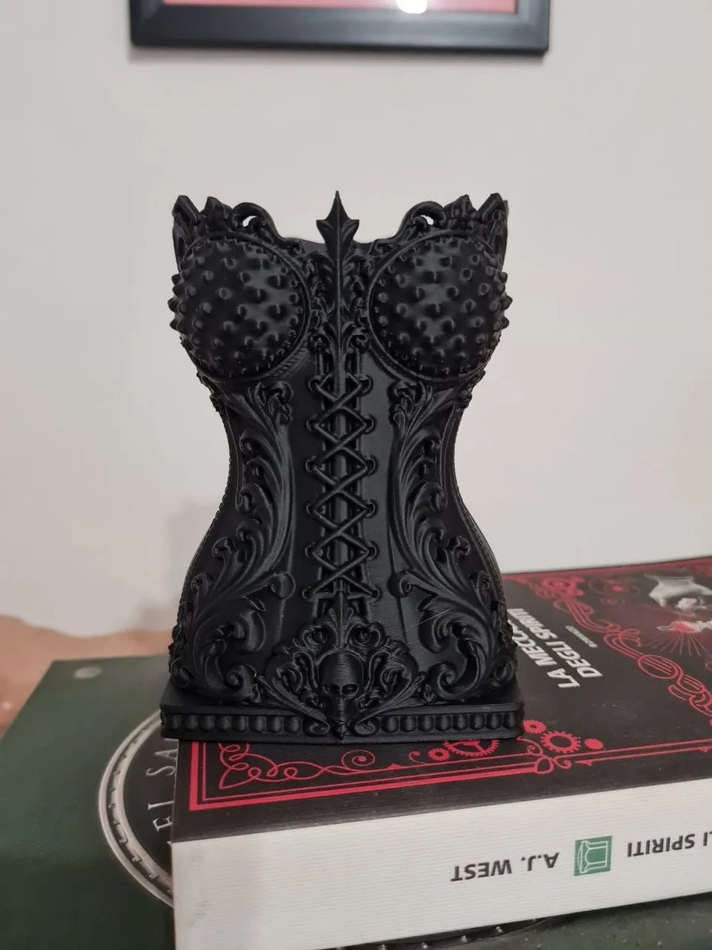 Echtes Foto des gedruckten Gothic-Korsett-Pinselhalters in Schwarz auf einem Bücherstapel