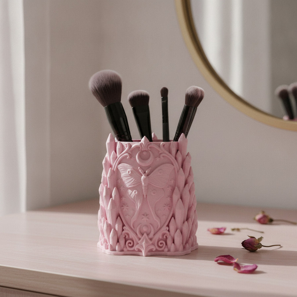 Rosa Gothic Kristall-Pinselhalter mit Luna-Motten-Relief, gefüllt mit Make-up-Pinseln auf einem hellen Schminktisch vor einem runden Spiegel