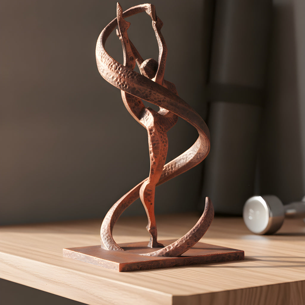 Gymnastik-Statue in Kupfer-Bronze-Optik auf Holzregal im Home-Gym, Dreiviertelansicht mit Bandwirbel, unscharfer Hintergrund mit Yogamatte und Kurzhantel – Münch3D