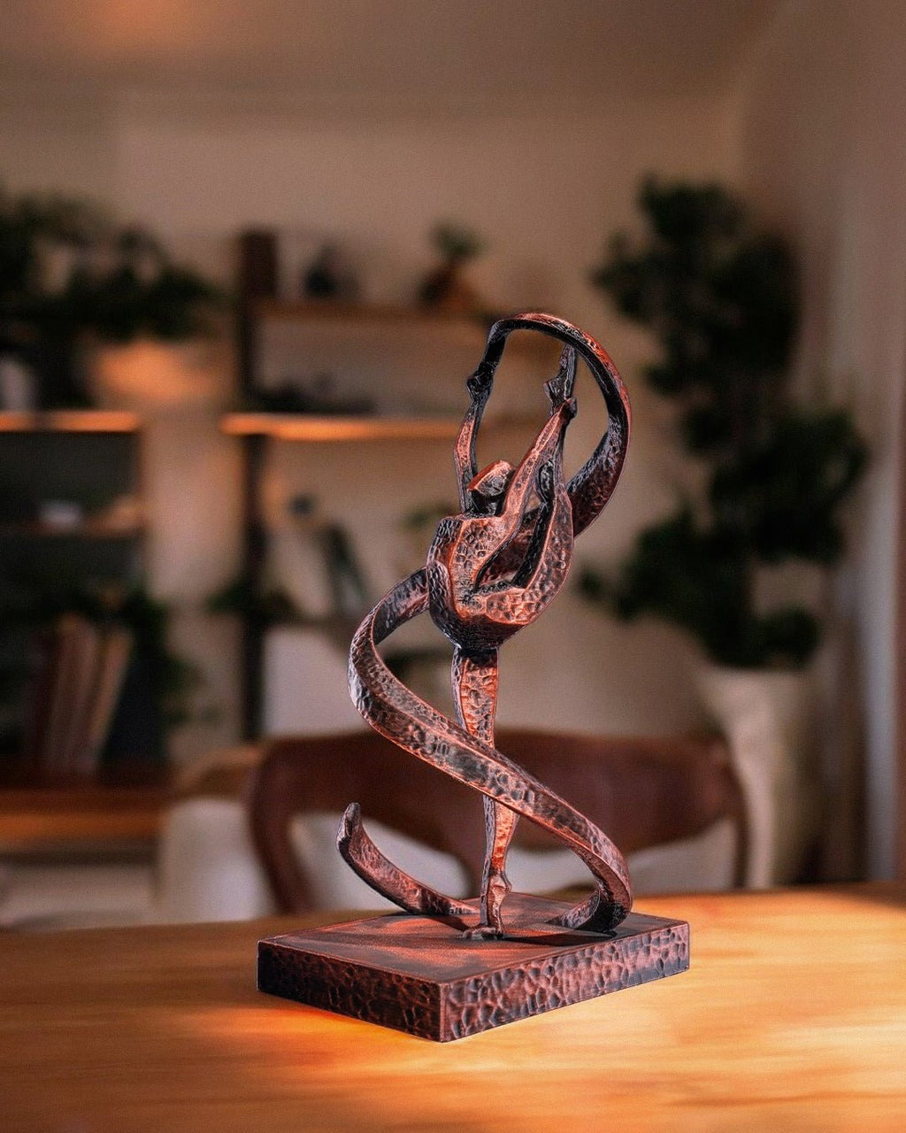 Handbemalte Gymnastik-Statue in Kupfer-Optik mit Bandwirbel, 3D-Druck im Wohnzimmer auf Holztisch, unscharfer Hintergrund mit Pflanzen und Regal – Münch3D