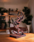 Handbemalte Gymnastik-Statue in Kupfer-Optik mit Bandwirbel, 3D-Druck im Wohnzimmer auf Holztisch, unscharfer Hintergrund mit Pflanzen und Regal – Münch3D