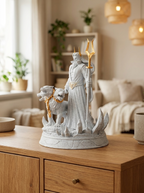 Hades-Statue mit zweizackigem Zepter, zwei der drei Cerberus-Köpfe aus diesem Winkel sichtbar, auf Holzkommode mit Bücherregal und Hängeleuchten im Hintergrund