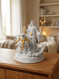 Hades-Statue Frontalansicht mit zweizackigem Zepter und dreiköpfigem Cerberus an goldener Kette, auf Felssockel mit Kristallzacken, auf Holzkommode mit Bücherregal im Hintergrund